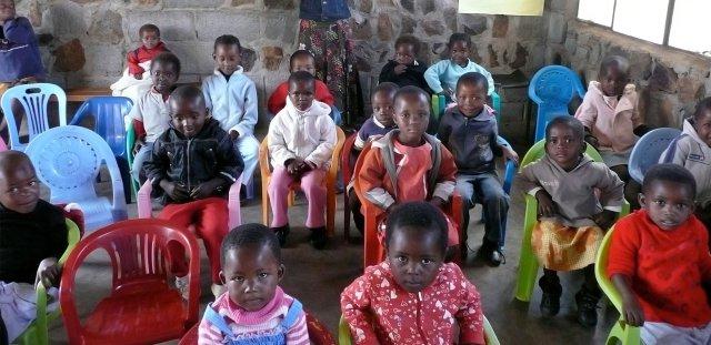 Little children sitting in chairs in classroom staring wide-eyed up at the camera