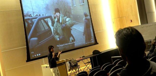 教授. Bohlinger lectures in front of class, with image of film behind him.