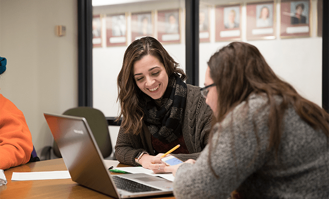 Two happy female students working on one laptop